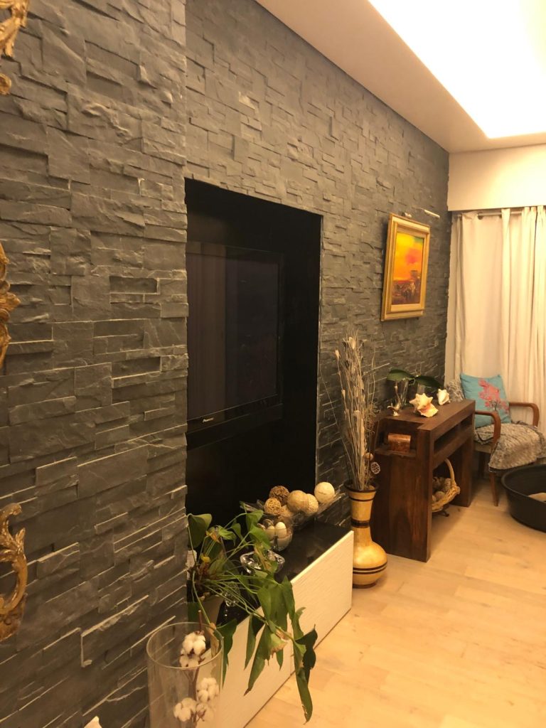 Salon avec mur en pierre décorative et niche intégrée ainsi que le sol, créant une pièce centrale chaleureuse réalisée par EDVA Rénovation